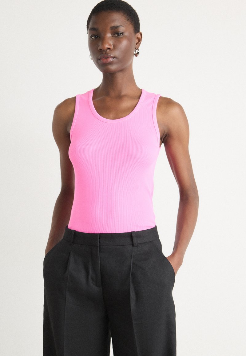 Rosa ribbet tank topp med rund hals, sammen med svarte høyhalsbukser med plisserte detaljer og sidelommer.