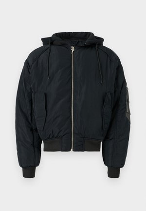 Veste bomber matelassée noire avec capuche, fermeture éclair à l'avant et poignets côtelés. Comprend deux poches latérales et une poche sur la manche pour le rangement.