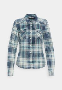 Chemise à carreaux à manches longues, présentant des nuances de bleu et de vert, avec une fermeture boutonnée à l'avant et deux poches poitrine. Fabriquée en tissu doux.