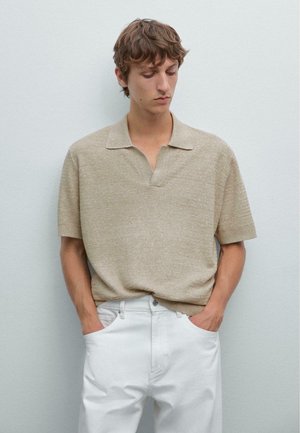 Beige gebreide poloshirt met korte mouwen en een open kraag, voorzien van een subtiele structuur, gecombineerd met witte, losvallende broek.