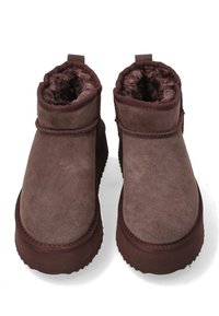 Brune ruskindsankelstøvler med en blød, fuzzy foring, rund tå og tekstureret gummisål. Har et enkelt design med minimal syning.