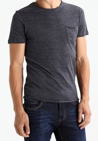 Dunkelgraues T-Shirt mit kurzen Ärmeln aus weichem Stoff, mit einer Brusttasche, schmaler Passform und Rundhalsausschnitt, kombiniert mit blauen Jeans.