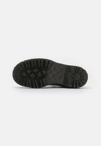 Suela de goma negra con un patrón de goma resistente, que presenta profundas ranuras y una superficie texturizada para mejorar la tracción y durabilidad.