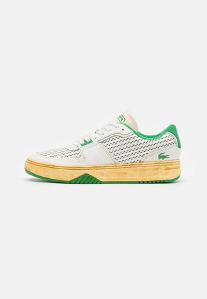 Baskets blanches et vertes avec côtés perforés, doublure intérieure verte, semelle jaunie et logo crocodile vert sur la zone du talon.