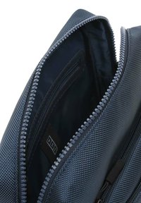 Borsa di tessuto blu con superficie testurizzata, dotata di chiusura con zip e tasca interna. L'interno è scuro e liscio.