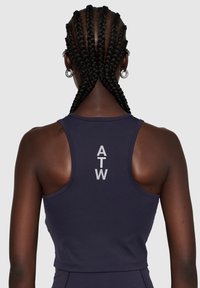 Marineblauwe sportcrop top met een racerbackdesign. Bevat het "ATW"-logo in het wit op de achterkant. Soepele textuur en een aansluitende silhouet.