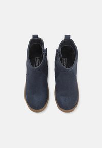 Granatowe zamszowe botki za kostkę o teksturowanej powierzchni, brązowe gumowe podeszwy i boczne zamki błyskawiczne, które ułatwiają zakładanie. Posiadają gładką, zaokrągloną sylwetkę.