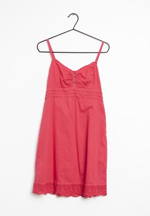 Korallenfarbene ärmellose Kleid mit tailliertem Oberteil, Knopfdetails, gerafftem Material und dekorativem Spitze-Saum. Hängt an einem schwarzen Haken.