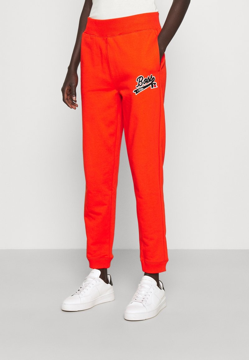 Klarröda sweatpants med ett brett elastiskt midjeband och sidofickor. Har svart broderad logotypdetalj på höften. Slät tyg.