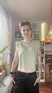 Light green cropped tank top with wide shoulders, made of soft fabric. Worn with high-waisted black pants, showcasing a casual look.