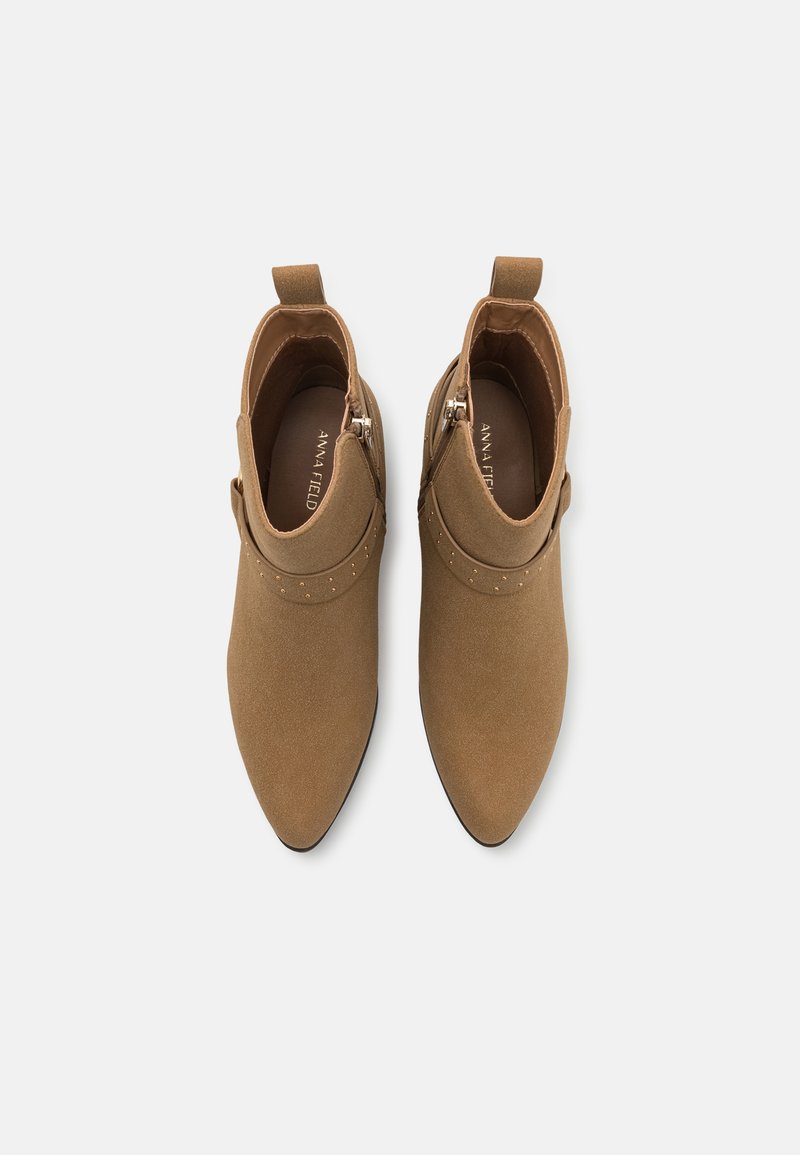 Botines tobilleros color marrón con un acabado de ante suave, puntera afilada, tachuelas decorativas en la parte superior y cremallera lateral para el cierre.