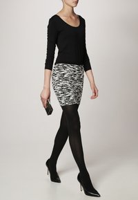 Zwarte lange mouwen top en een gestreepte zwart-wit minirok. Zwarte panty's en puntige hakken. Een kleine rechthoekige clutch in de hand.