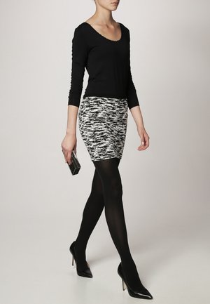 Haut à manches longues noir et mini-jupe noire et blanche à motifs. Collants noirs et escarpins à bout pointu. Une petite pochette rectangulaire à la main.