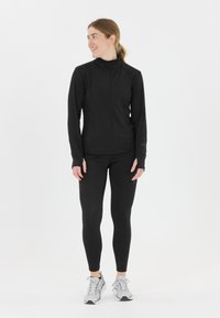 Sort sportsjakke med lange ærmer og høj krave, parret med sorte leggings. Tekstureret overflade, designet til aktivt tøj.