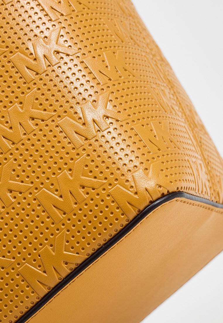 Gelbe Lederhandtasche mit geprägtem MK-Logo-Muster, feinen Perforationen und einem glatten Boden mit kontrastierenden Kantenverzierungen.