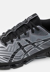 Scarpa atletica nera e grigia con tomaia in rete testurizzata, motivo grafico audace e lacci neri. Presenta una suola imbracata per un supporto ottimale.