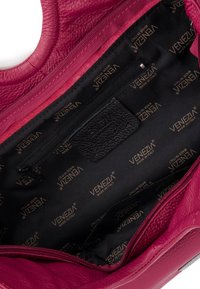 Sac à main en cuir rose avec un extérieur texturé, une poche zippée à l'intérieur et une doublure en tissu noire avec impression en or du logo.