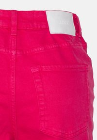 As calças de ganga cor-de-rosa apresentam um bolso traseiro, detalhes cosidos e uma etiqueta de tecido branca com a inscrição "JJXX" na cintura. Textura suave e design ajustado.