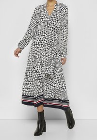 Långärmad omlottklänning i svart och vit hounds-tooth-mönster, med en djup v-ringning och en randig nederdel i marinblått, rött och vitt.