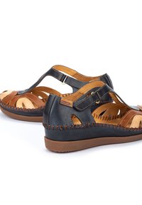Sandales en cuir bleues et brunes, avec des découpes, des accents de couture et une semelle en caoutchouc flexible pour le confort.