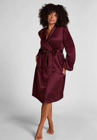 Burgunderröd satinrock med långa ärmar, omlottmodell och justerbart knytband i midjan. Slät yta med knälång längd.