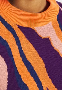 Jersey de punto con un cuello acanalado naranja, con un patrón de olas en morado, naranja, rosa y azul marino a lo largo de la tela.
