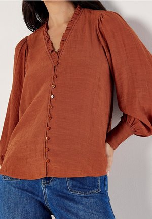 Langærmet bluse i rustfarve med små knapper ned foran, flæset krave, puffede ærmer, båret med blå denimjeans.