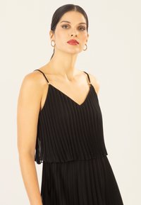 Schwarzes, plissiertes Kleid mit verstellbaren, dünnen Trägern und goldenen Hardware-Details, das ein geschichtetes Design und eine fließende Textur aufweist.