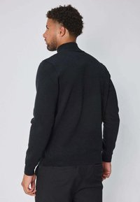 Pull en tricot noir avec des manches longues et un col haut. Texture douce, design minimaliste et coupe ajustée.