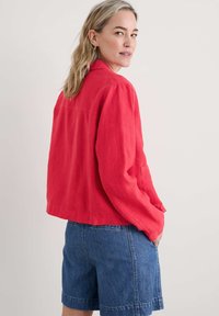 Giacca in lino rossa con una vestibilità rilassata, caratterizzata da maniche lunghe e tasche laterali, abbinata a pantaloni shorts in denim blu. Design semplice e texture morbida.