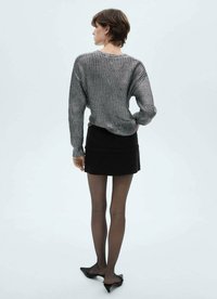 Siva rebrasta pletena bluza z ohlapnim krojem, v kombinaciji z črno mini krilom. Model nosi prozorne črne nogavice in črne špici čevlje.