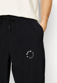 Zwarte sportbroek van een gestructureerde stof, voorzien van een elastische tailleband met een trekkoord en een cirkelvormig logo met de tekst "7 DAYS ACTIVE."
