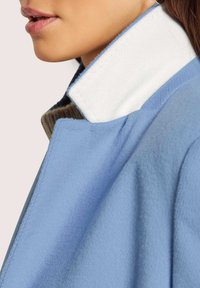 Helle blaue Jacke aus strukturiertem Stoff mit kontrastierendem weißen Kragen. Sie verfügt über einen sauberen Schnitt und ein maßgeschneidertes Design. Nahaufnahme des Kragens.