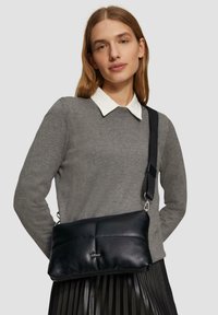 Schwarze Ledertasche mit einem gesteppten Design und silberner Hardware. Verfügt über einen abnehmbaren Trageriemen und eine glatte Textur.