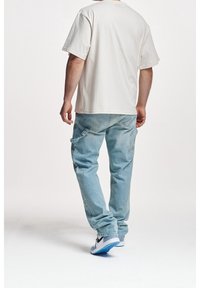 Light beige oversized t-shirt paired with light blue cargo jeans featuring side pockets, completed with white and black sneakers.