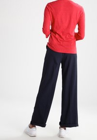 Haut rouge à manches longues associé à un pantalon large à rayures bleu marine et des baskets blanches, montrant une coupe décontractée et confortable.