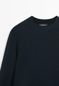 Donkerblauwe gebreide trui met een ronde halslijn, met raglanmouwen en een zachte textuur. Label zichtbaar bij de halslijn.
