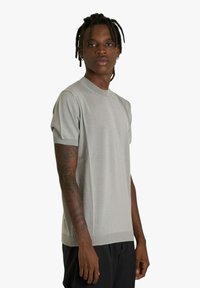 Maglia a maniche corte color grigio chiaro con scollo a girocollo e polsini a coste, caratterizzata da una texture liscia e una vestibilità rilassata.