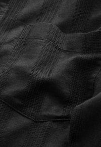 Tissu noir avec des rayures texturées verticales, présentant des tissages variés. Texture douce avec un léger éclat, montrant des coutures et des bords détaillés.