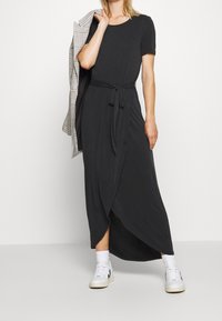 Mustassa maksimekossa on pehmeä kangas, pyöreä pääntie, lyhyet hihat, kireä vyötärö soljella ja sivuhalkio.