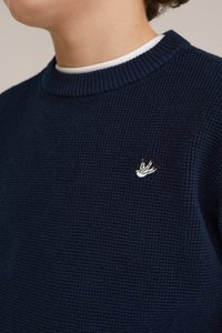 Marinblå stickad tröja med ribbade detaljer vid halsringningen och en liten broderad logotyp på bröstet. Strukturerad tyg med en klassisk design.