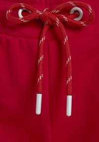 Red pants featuring a smooth texture, an elastic waistband, and a drawstring with white accents, ending in plastic aglets.
