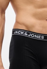 Ανδρικός κορμός που φοράει μαύρα εσώρουχα με την ένδειξη Jack & Jones και ελαστική μέση, ορατά σε απλό φόντο.