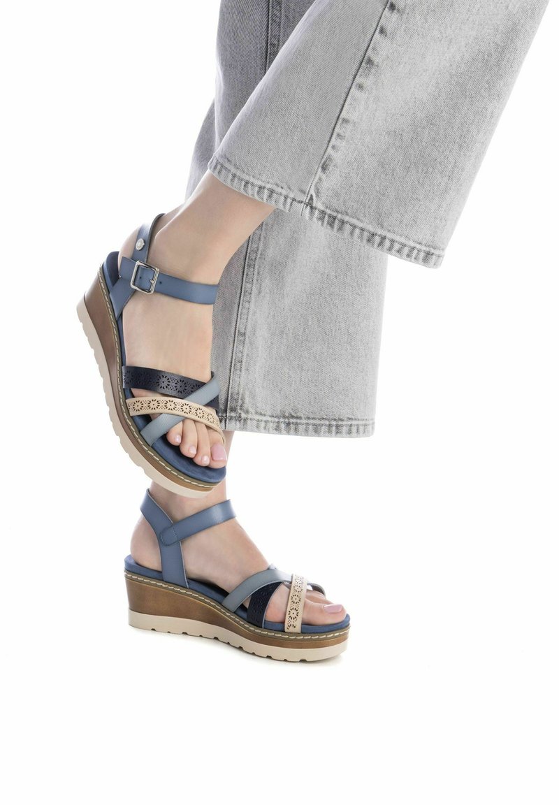 Sandalias de cuña azules con múltiples correas, incluyendo una correa perforada de color marrón claro. Cuenta con una suela texturizada y una plataforma de color claro.