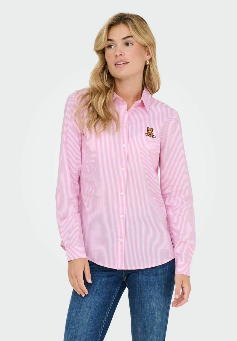 Camisa de botones a rayas rosas con cuello y bordado de un oso en el lado izquierdo del pecho, combinada con jeans. Material de algodón y mangas largas.