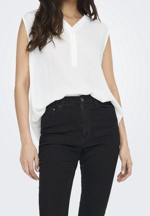 Vit ärmlös blus med V-ringning och knappdetaljer, ihop med högmidjade svarta jeans som visar en avslappnad passform och mjuk textur.