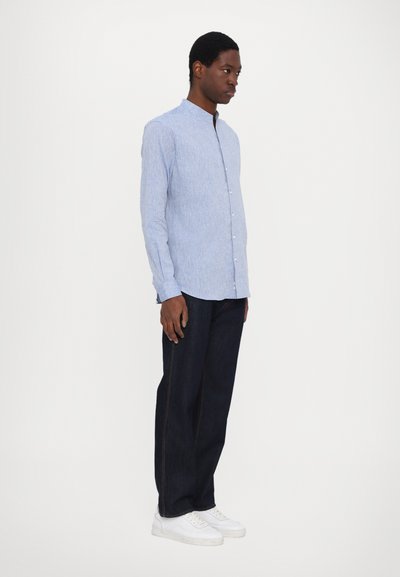 Ljust blå, långärmad skjorta med knappar och mandarinkrage, med ett subtilt randmönster; kombinerat med mörka jeans och vita sneakers.