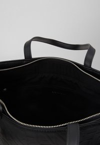 Svart skinn totebag med preget logo-mønster, glidelås-lukking og to solide håndtak. Innvendig foret med svart stoff med en glidelåslomme.