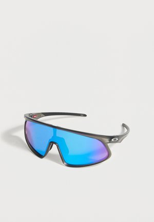 Lunettes de sport avec verres bleus réfléchissants enveloppants et monture noire reposant sur une surface blanche.