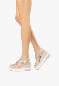 Beige wedge sandals with dual crisscross straps, a side buckle, and a textured sole. Features a white platform base and smooth finish.